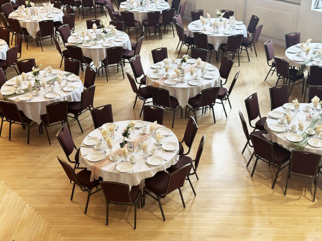 Banquet hall with a wood floor, multiple tables of 8 set with peach and sage green decorations in the Ballroom of the Polish Hall in Edmonton, AB