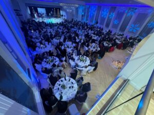 A beautiful view of the Grand Ballroom at full capacity in the Polish Hall, a Christmas party with snowflakes projected onto the wall and soft blue lighting.