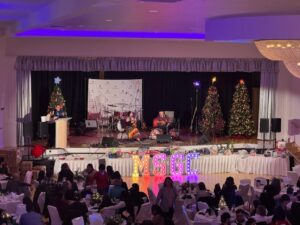 A corporate Christmas party in the main ballroom, featuring our stage with Christmas trees, and guest decor and band.
