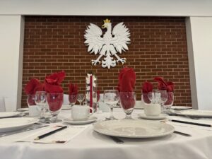 A beautiful table set with red napkins and an orchid centrepiece against a brick wall featuring the Polish Eagle carving in Syrenka.